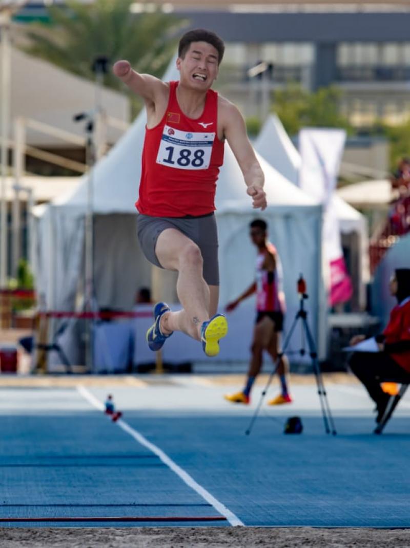 A one-armed man jumping in a long jump competition in a blue athletics track