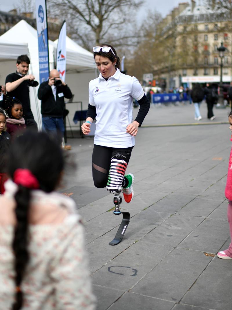 A woman with a prosthetic leg running in a square in the middle of a group of children and adults