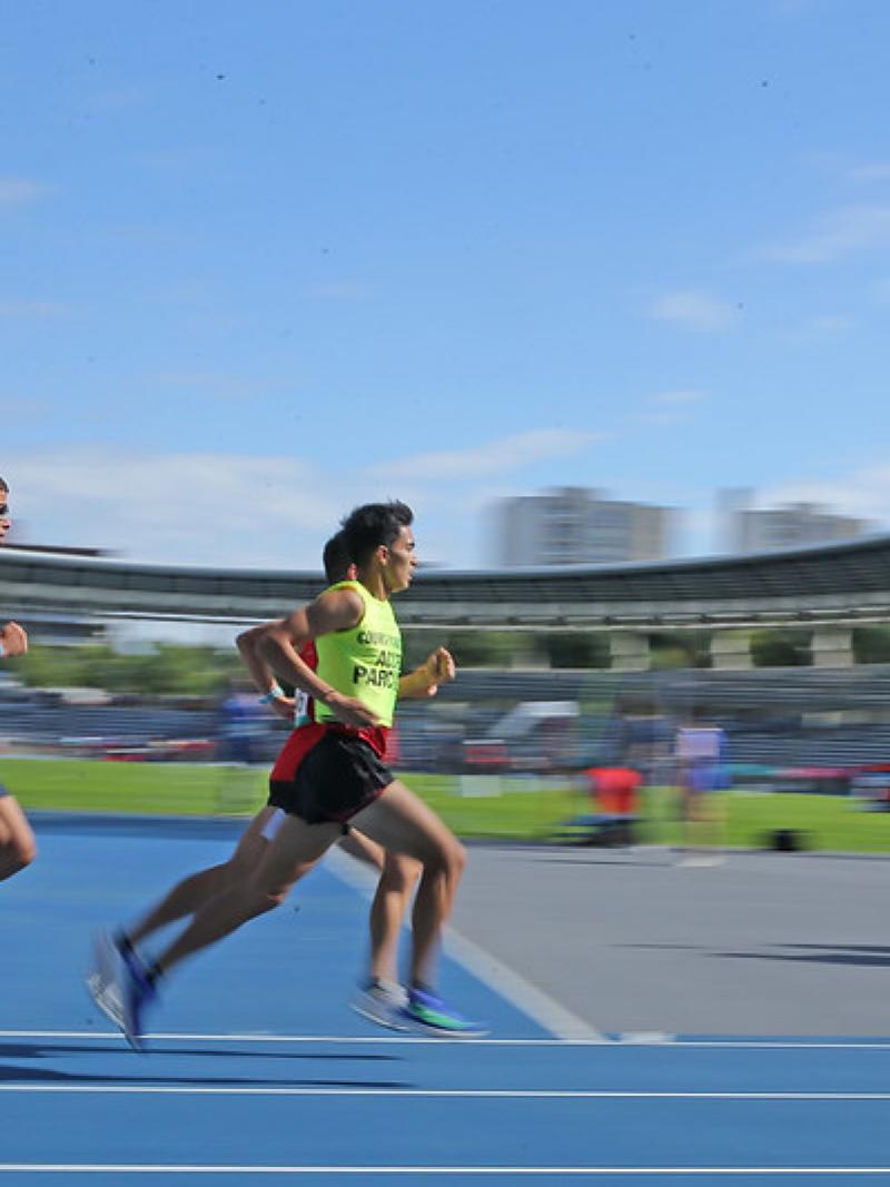 Three men running in a blue athletics track during a Para athletics event at Charlety Stadium in Paris