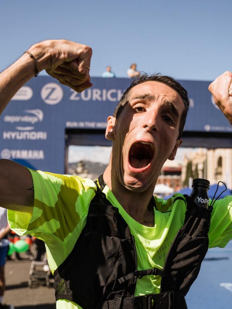 A male runner with cerebral palsy raises his hands in the air at the finish line of the Barcelona Marathon.