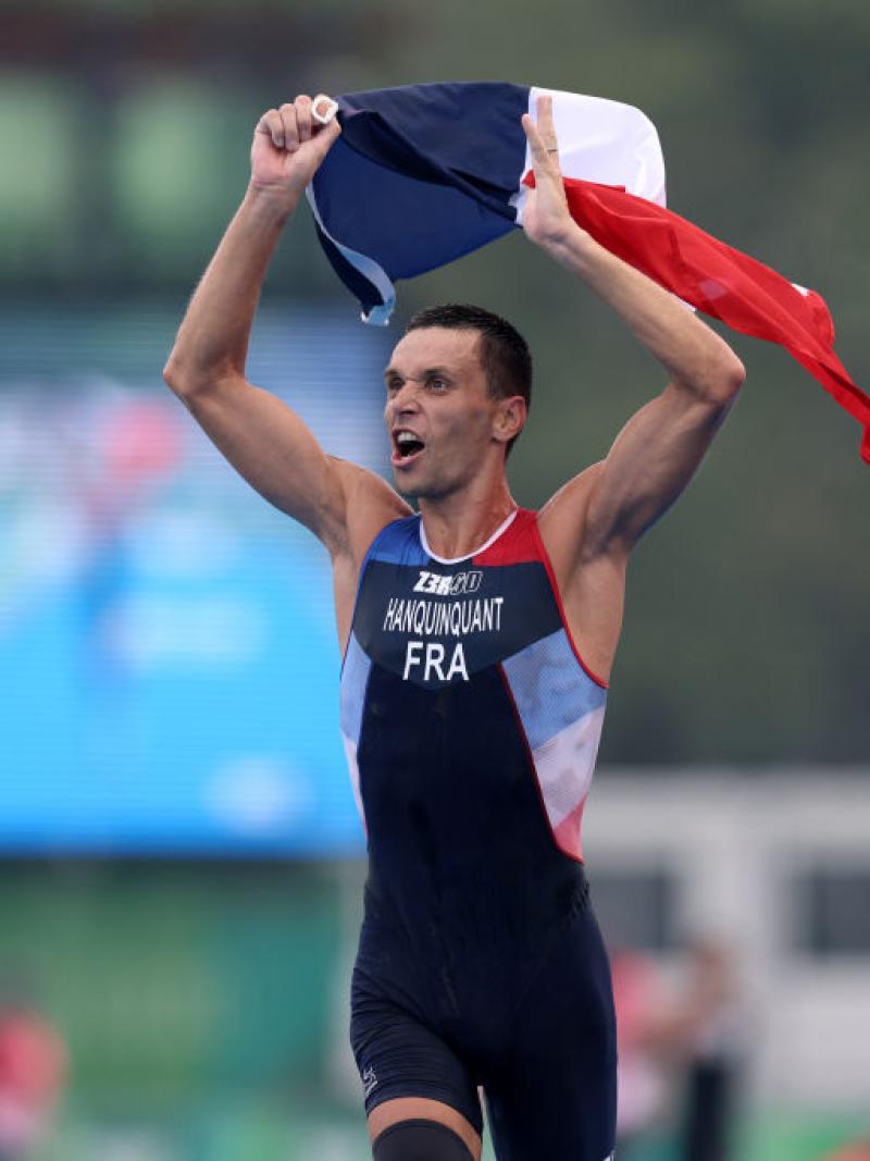 A male Para triathlete reacts to his victory at the Tokyo 2020 Paralympic Games by waving the French flag in the air.