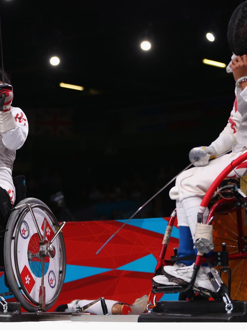 A female wheelchair fencer celebrates by taking her mask off with a shout after a winning bout.