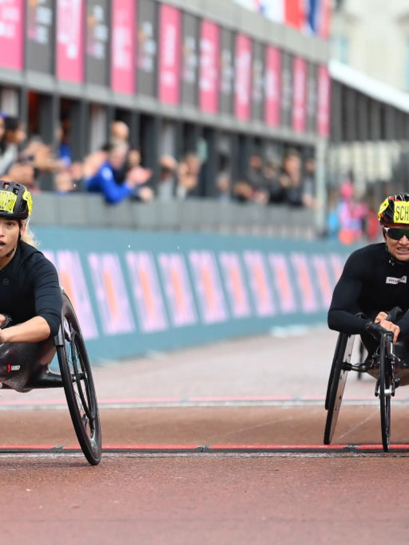 A female wheelchair racer crossing the finish line ahead of another racer in a street marathon