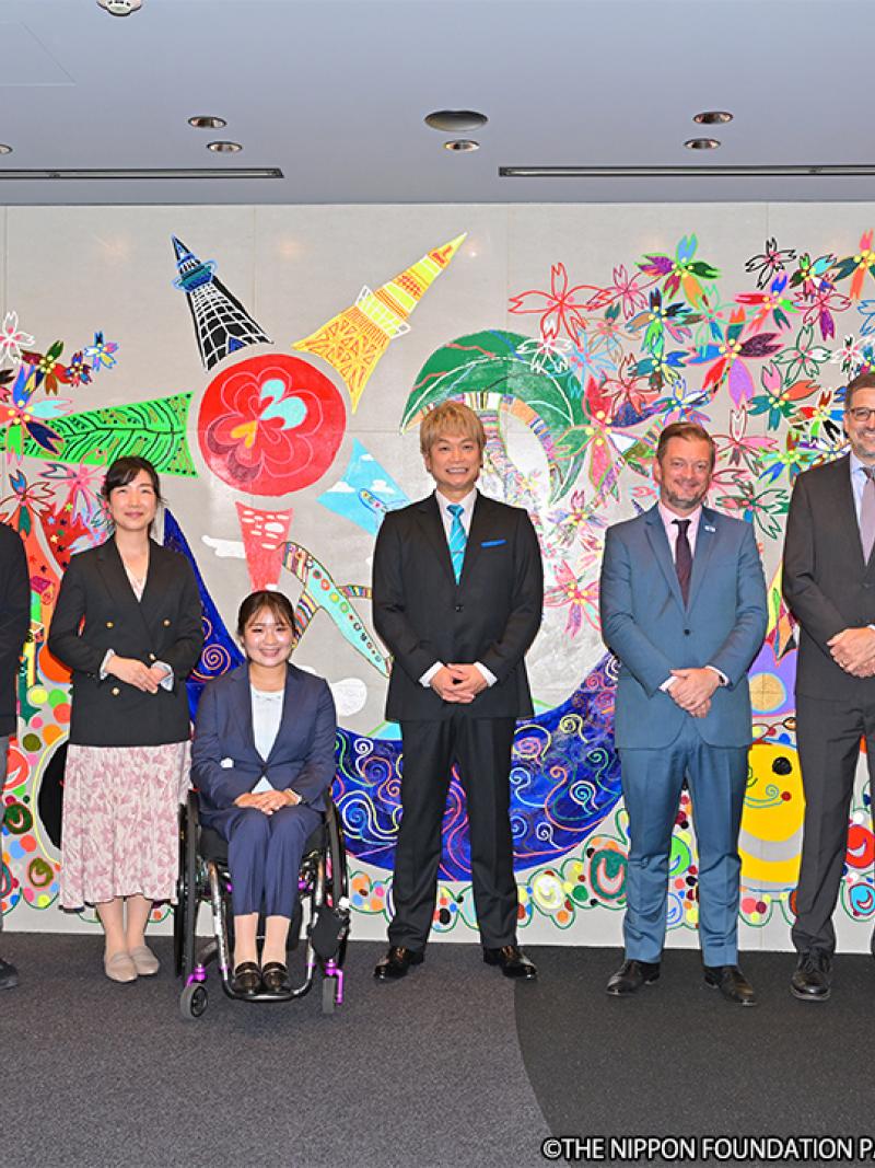 Seven people pose for a photograph in front of an artwork.