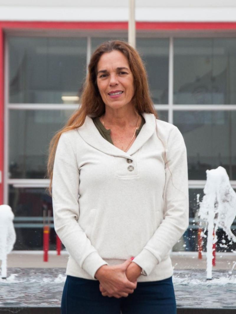 A woman poses for a photo in front of a fountain with her hands clasped together.