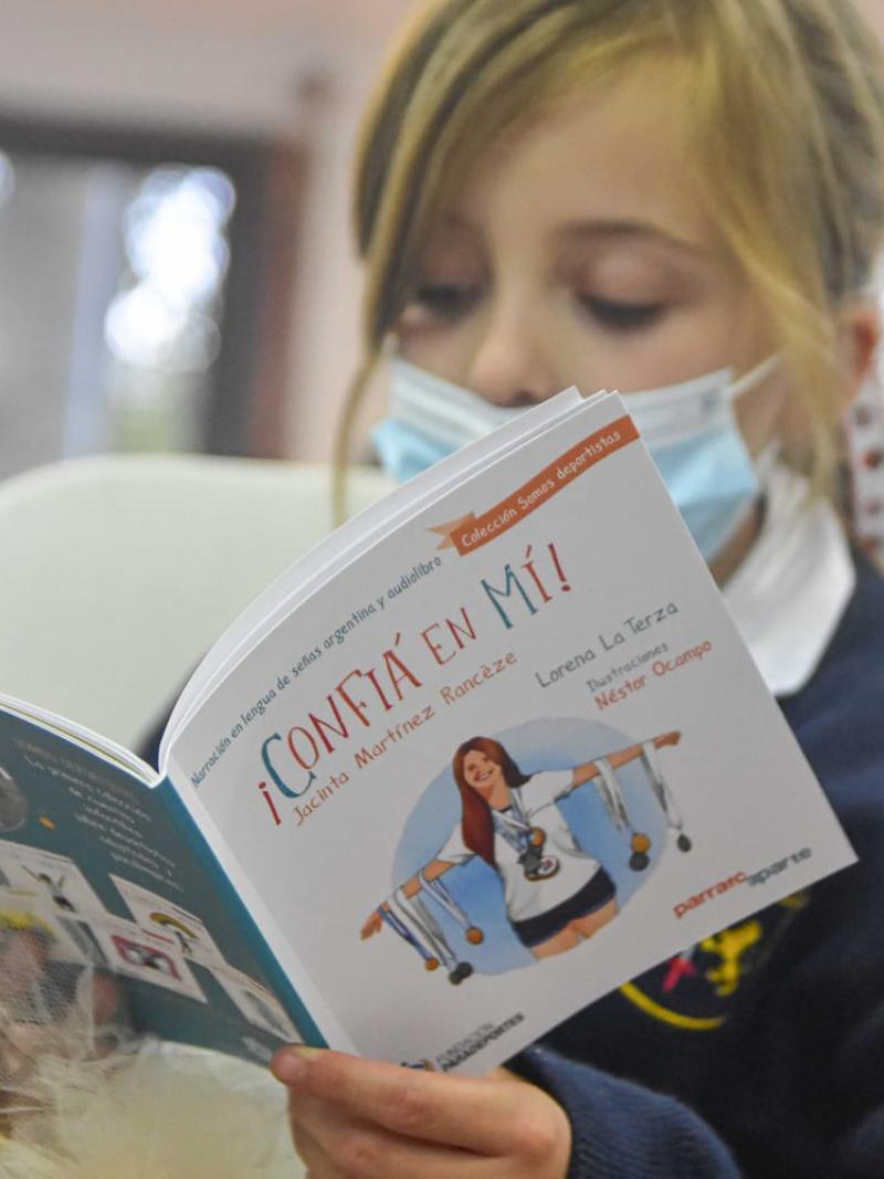A young girl reads a children's book with a Para athlete on the cover.