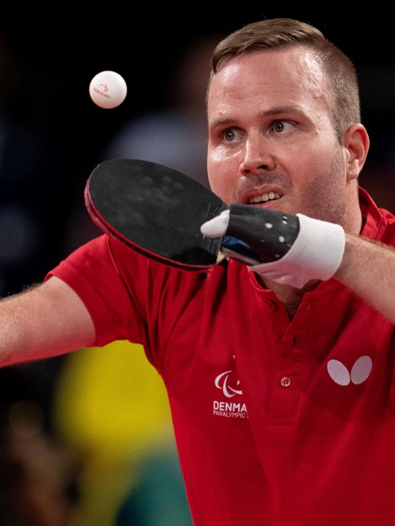 A male athlete wearing a red T-shirt plays table tennis