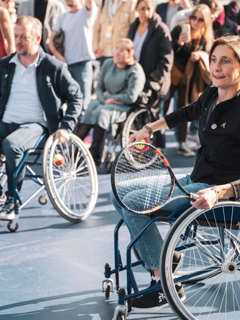 A woman and a man on a wheelchair holding tennis racquet.