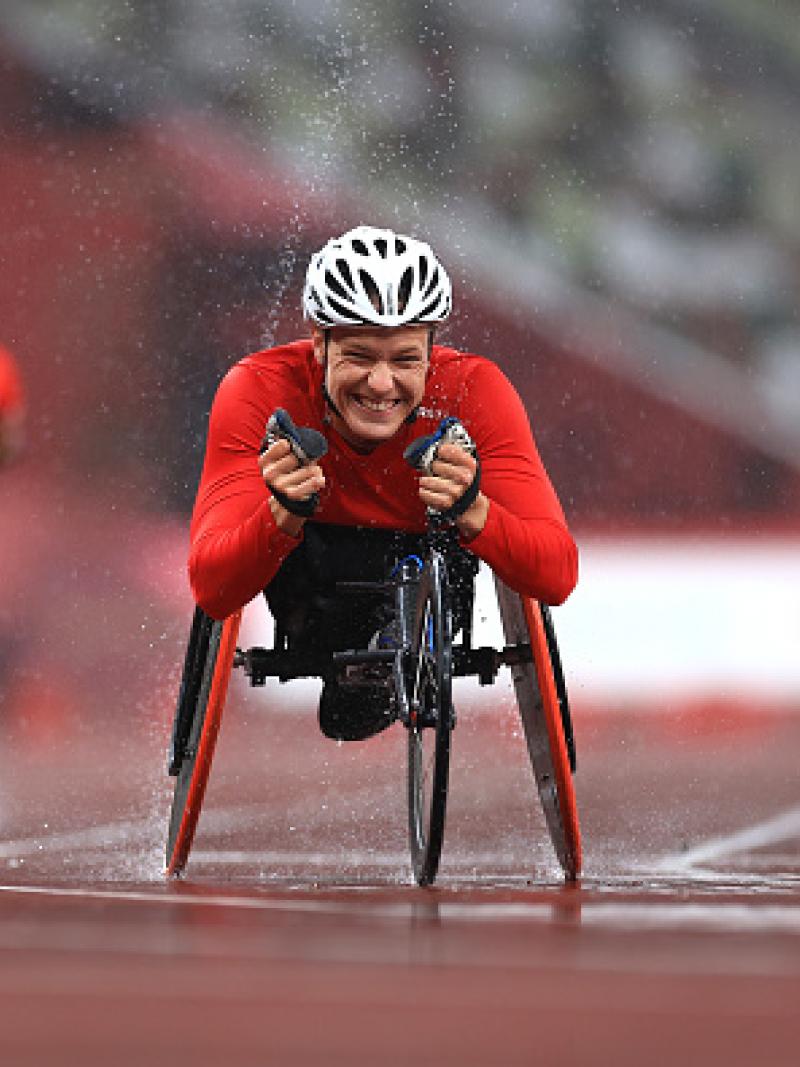 A female wheelchair racer celebrating ahead of two other racers