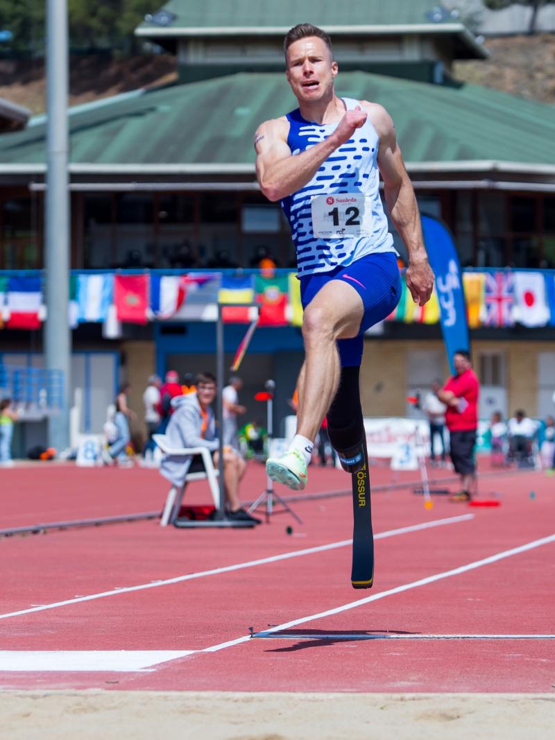 A male long jumper jumping with a prosthetic right leg