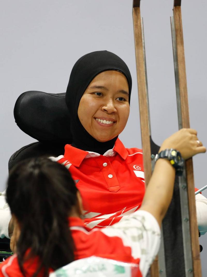 A female boccia athlete looks at her boccia ramp, while her assistant holds it.