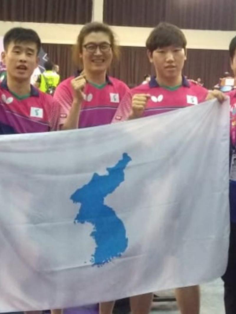 a group of Korean table tennis players standing with a United Korea flag