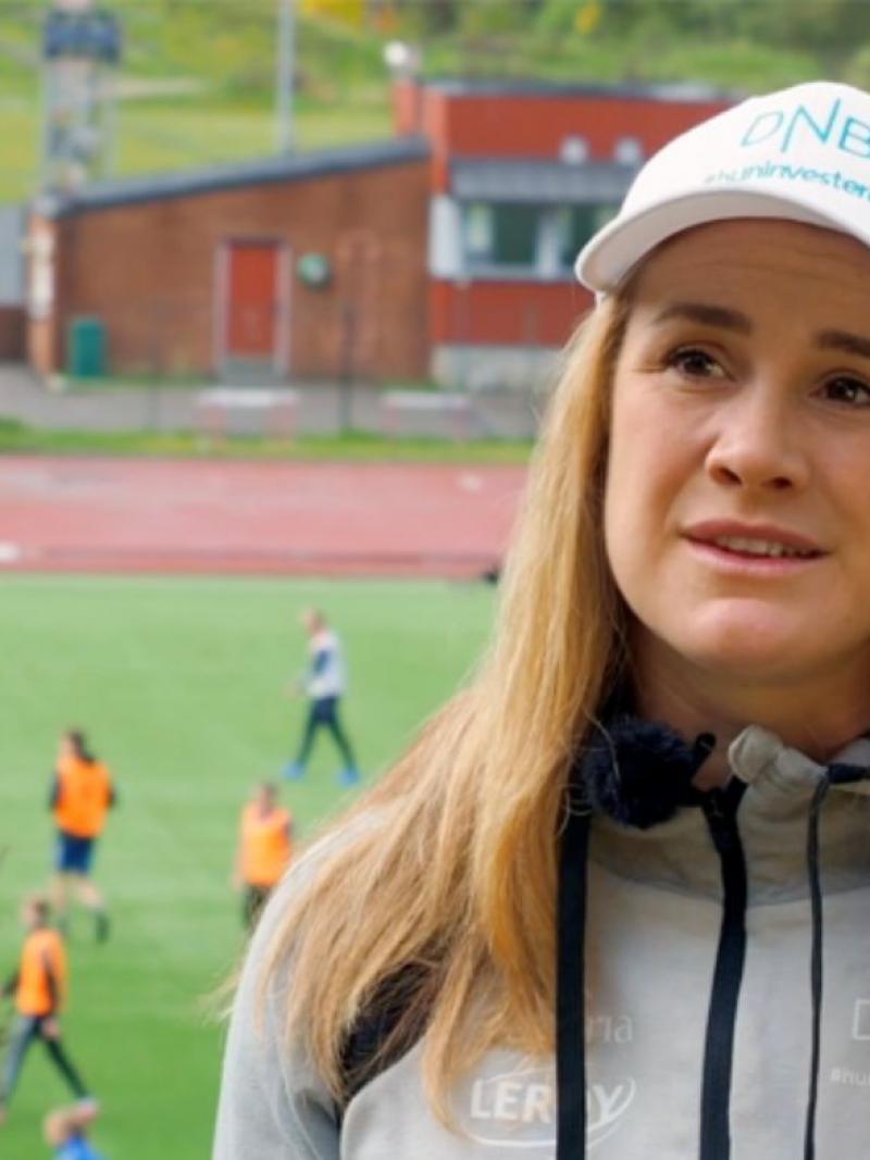A woman with a white cap talking with a football match in the background