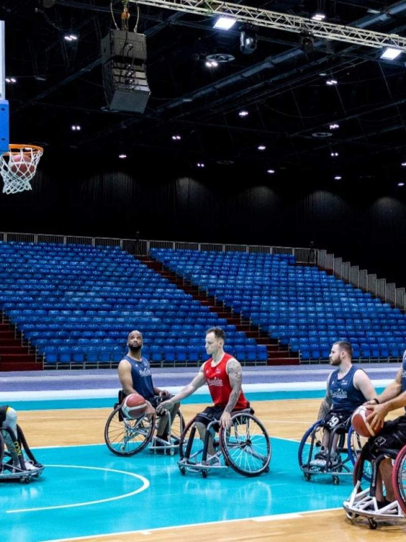 Six wheelchair basketball players train at an indoor hall.