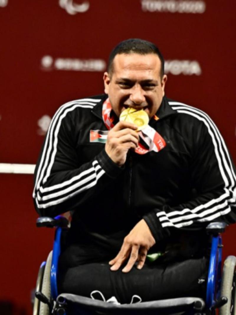 A man in a wheelchair biting his gold medal