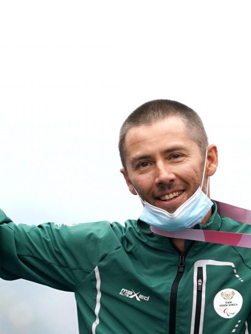 A male athlete raises his right arm in celebration while holding a gold medal with his left hand.