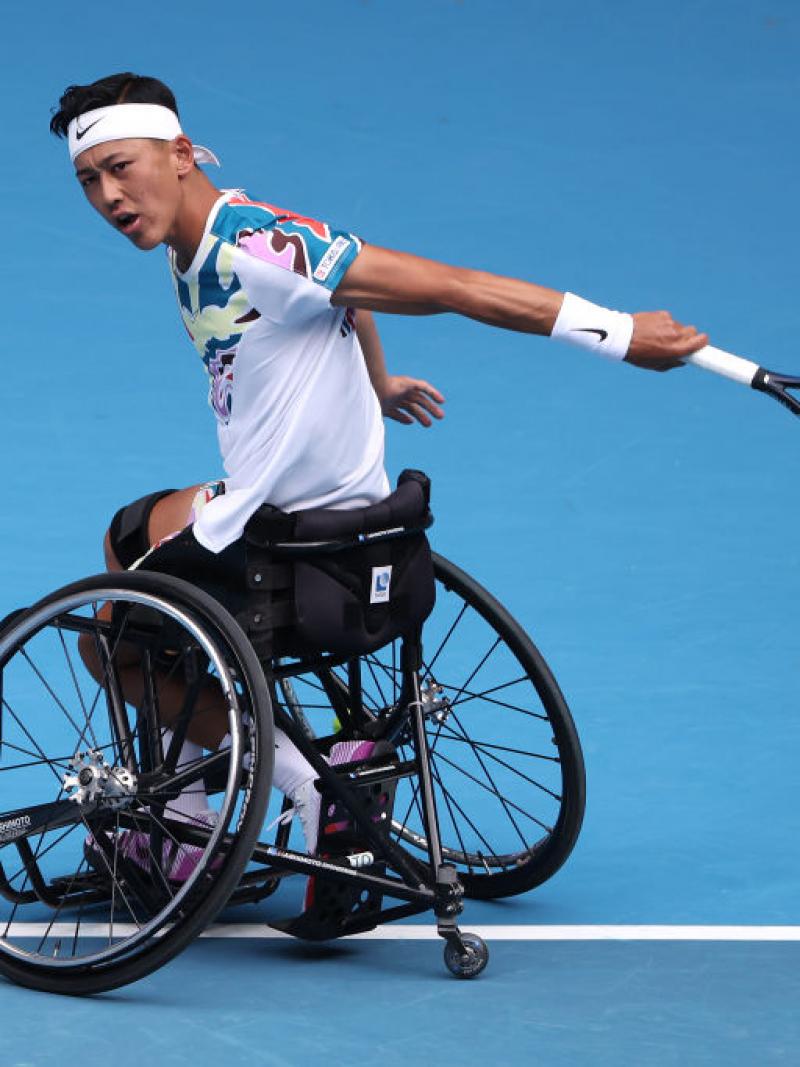 A male wheelchair tennis player hits a ball.