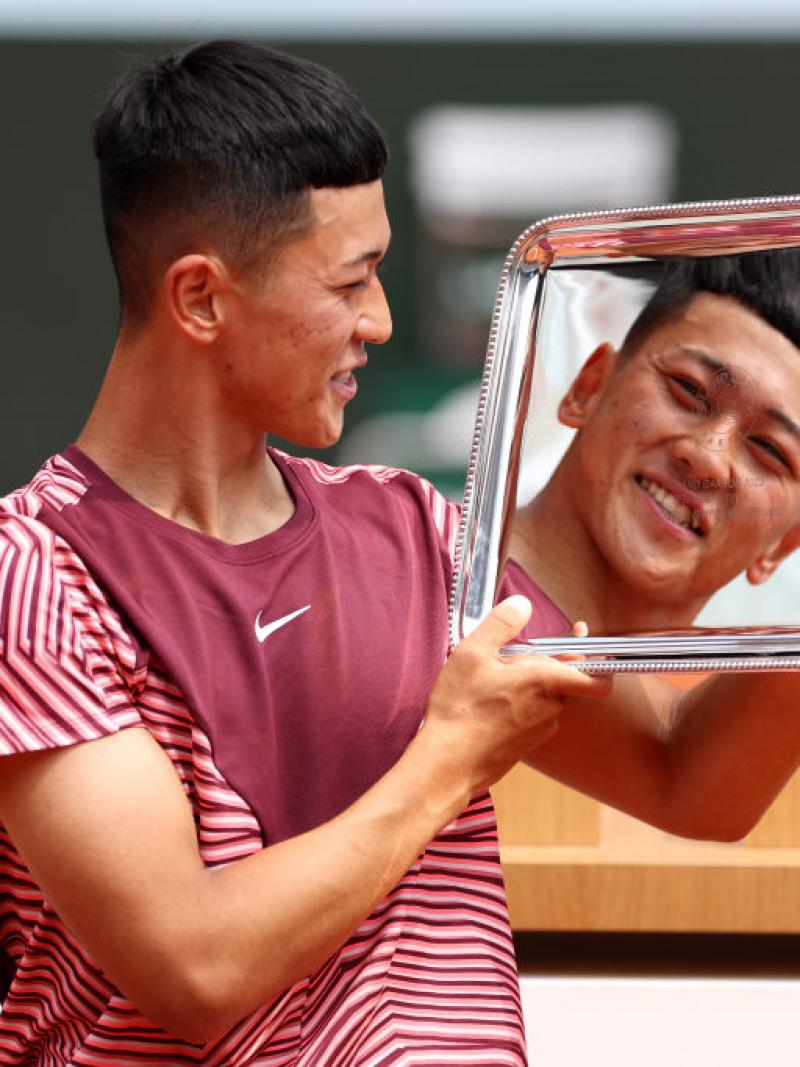 A male athlete holds the French Open trophy. His face is reflected on the silver trophy. 