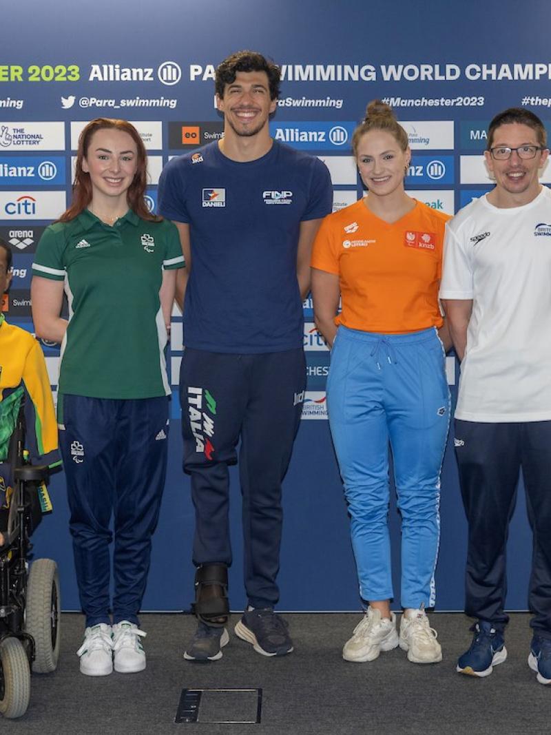 A male wheelchair posing for a picture next to a woman and a group of two men and other two women