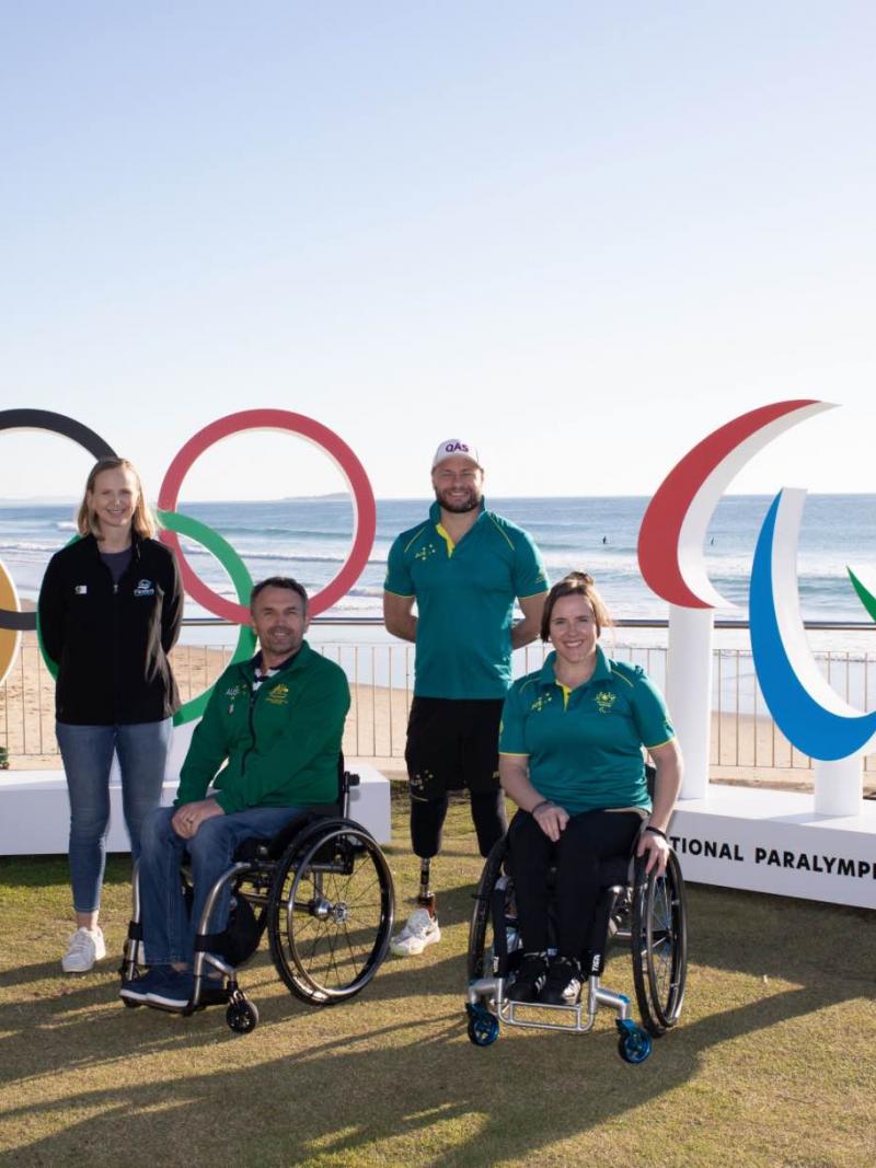 two wheelchair athletes and two athletes with prosthetics standing in front of the Paralympic and Olympic symbols 