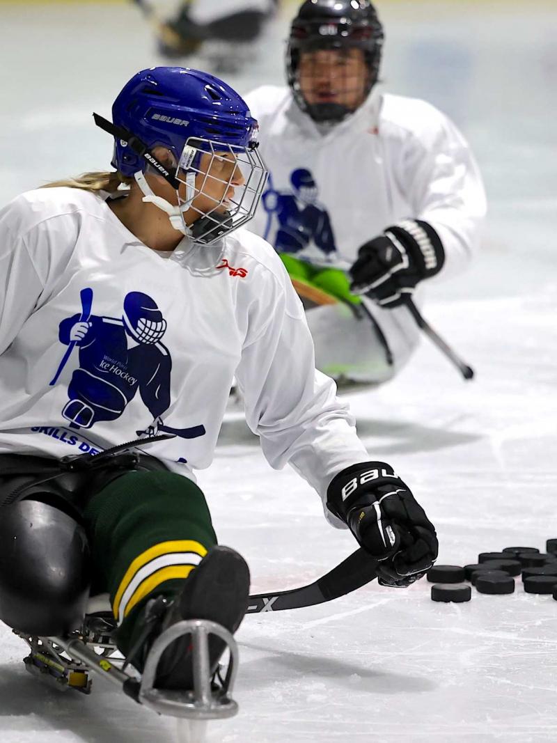A female Para ice hockey player on an ice rink followed by a male player