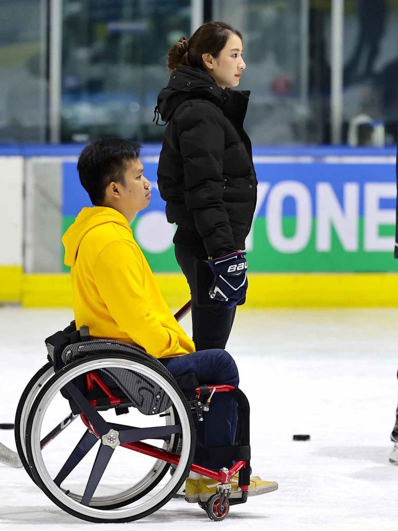 A man in a wheelchair next to a standing woman and a man on an ice rink