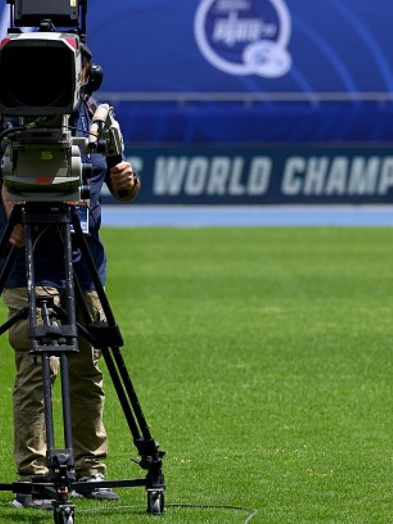A TV camera on a grass pitch in an athletics stadium