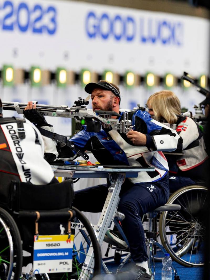 A group of five male and female rifle shooters in wheelchairs in a shooting range