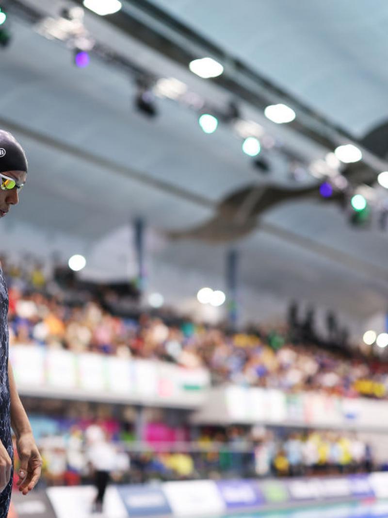 A female swimmer standing next to a pool in a crowded venue