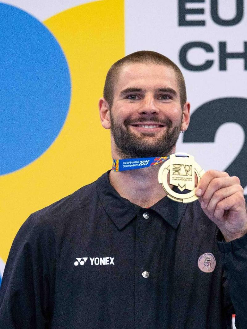 Para badminton player Lucas Mazur holding up his gold medal and smiling