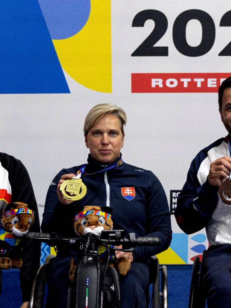A woman in a wheelchair between two men on a podium