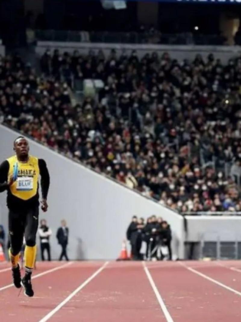 A male sprinter and a female sprinter run on the track of a packed stadium while holding relay batons.