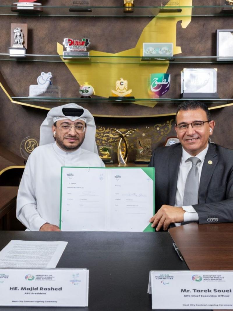 Two men sit next to each other holding a contract