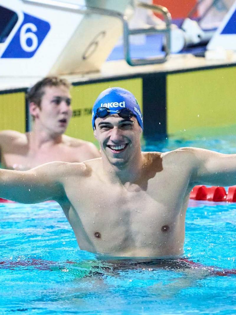 A male swimmer with his arms stretched in a pool with another swimmer in the background