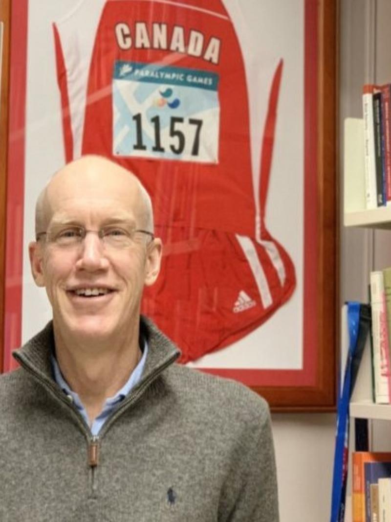 A man smiles in front of a book shelf.