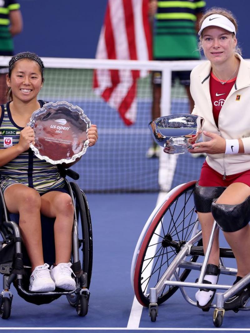 Two female wheelchair tennis athletes pose for a photo on the tennis court with their silverware