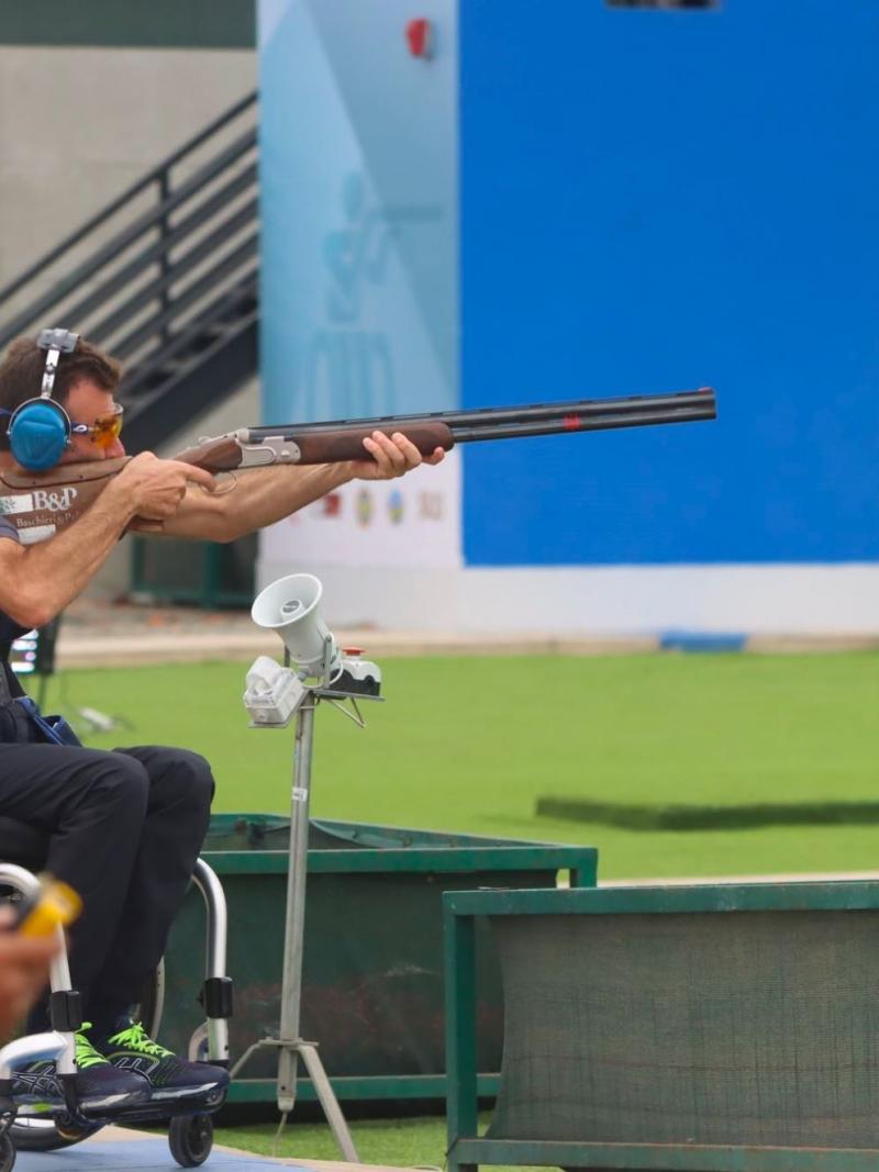 A man in a wheelchair in an outdoor Para trap shooting event