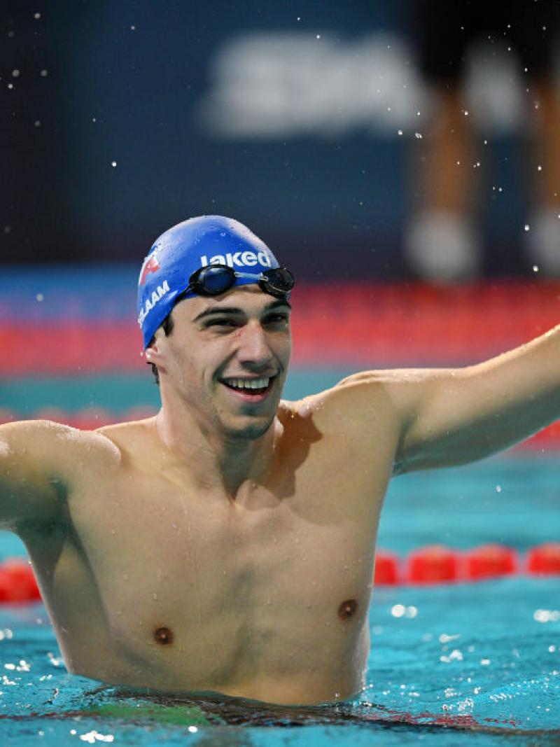 A male swimmer raises both hands in the pool to celebrate his victory.