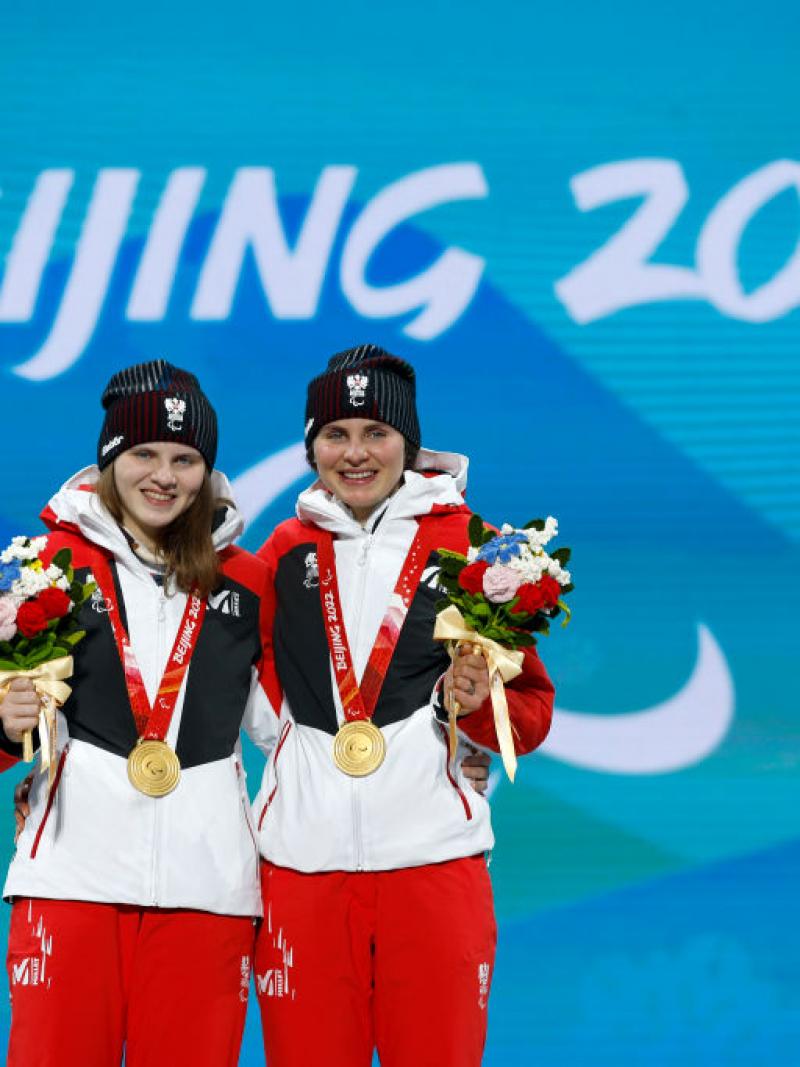 Two female athletes smile for a photograph after receiving gold medals.