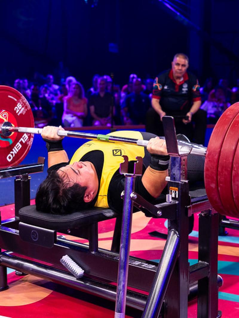 A short stature man lifting a bar in a Para powerlifting competition