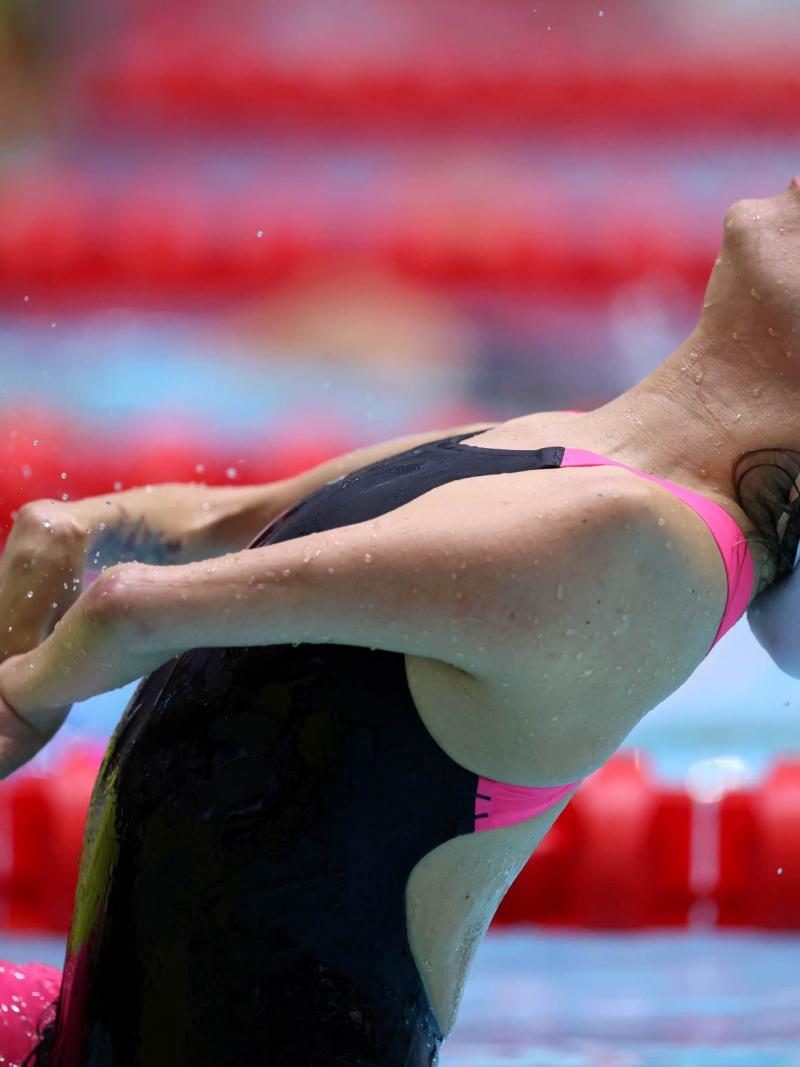 A female swimmer jumping in the water in a backstroke race