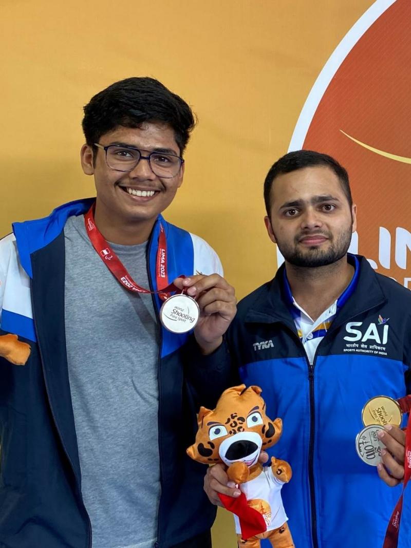 Two athletes holding medals and a mascot plush toy