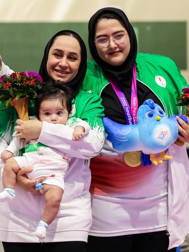A woman with a headscarf holding a baby next to another woman with a headscarf in a shooting range