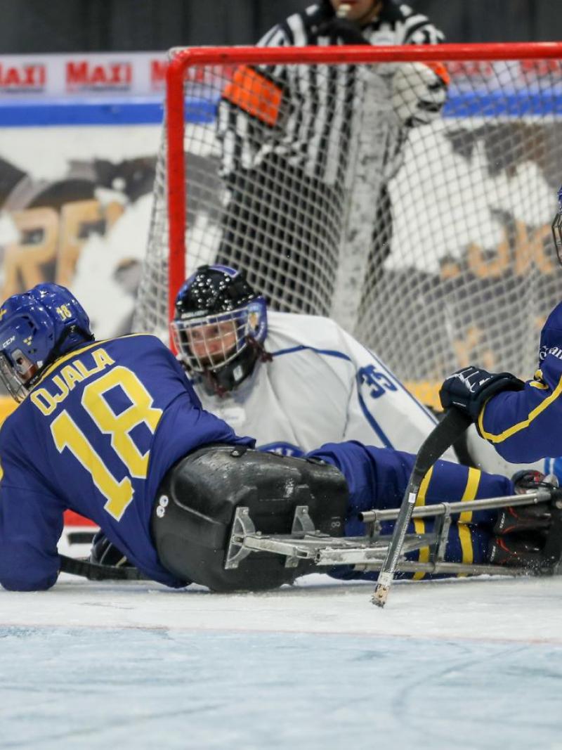 Two Swedish players in front of the Finnish goaltender in a Para ice hockey game