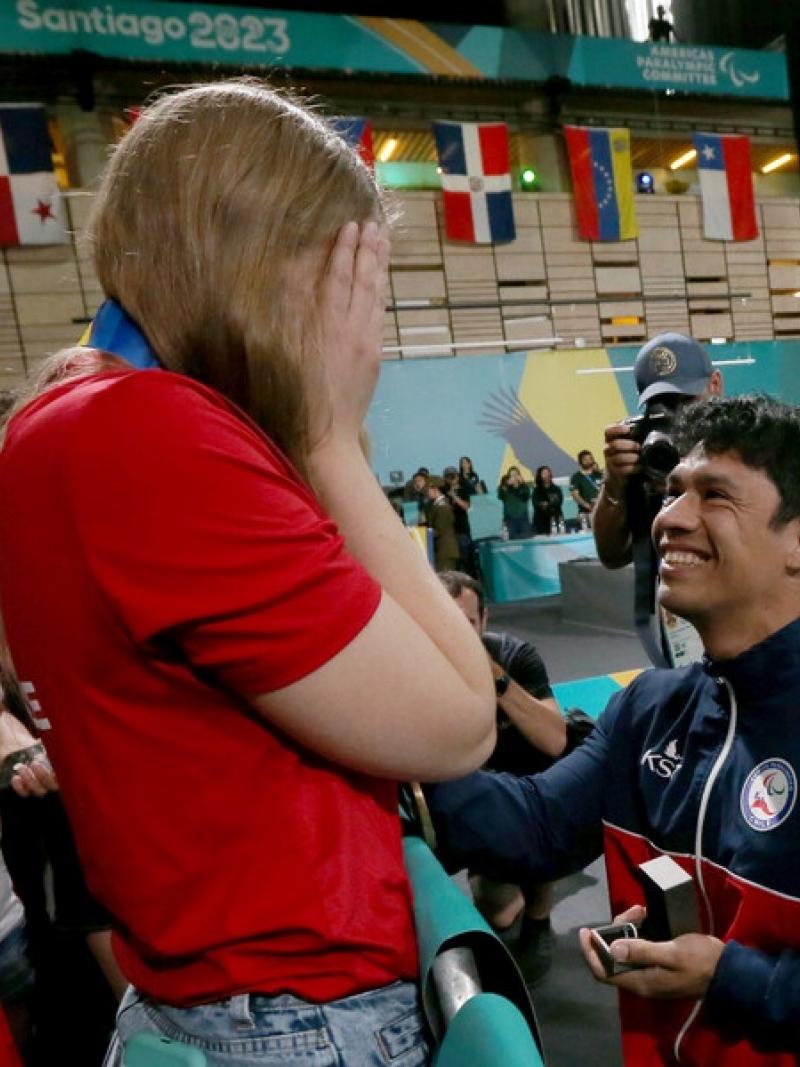 A man in a wheelchair proposing to a standing woman in a competition arena