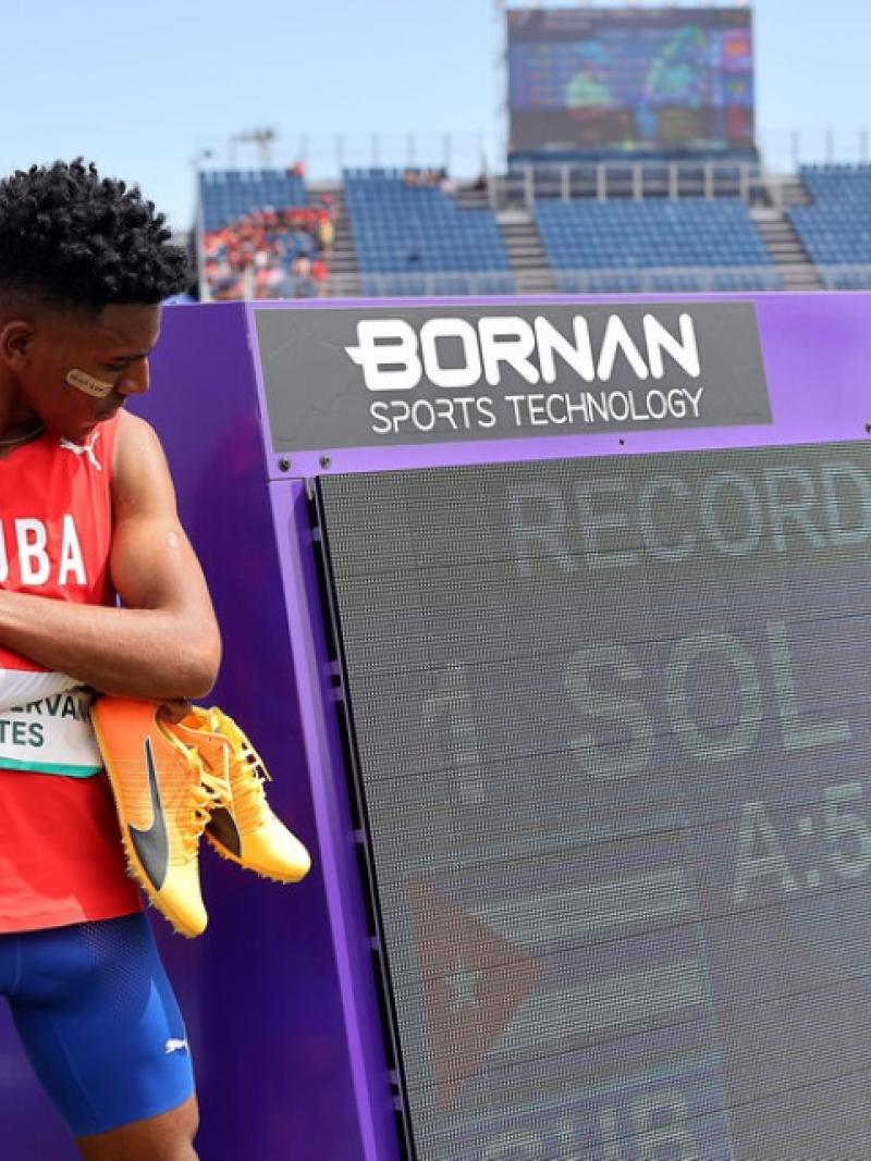 A man standing next to a screen showing his world record on an athletics field