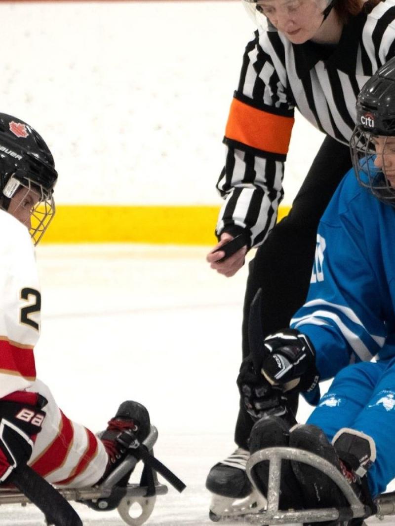 A Para ice hockey official throwing a puck between two female players