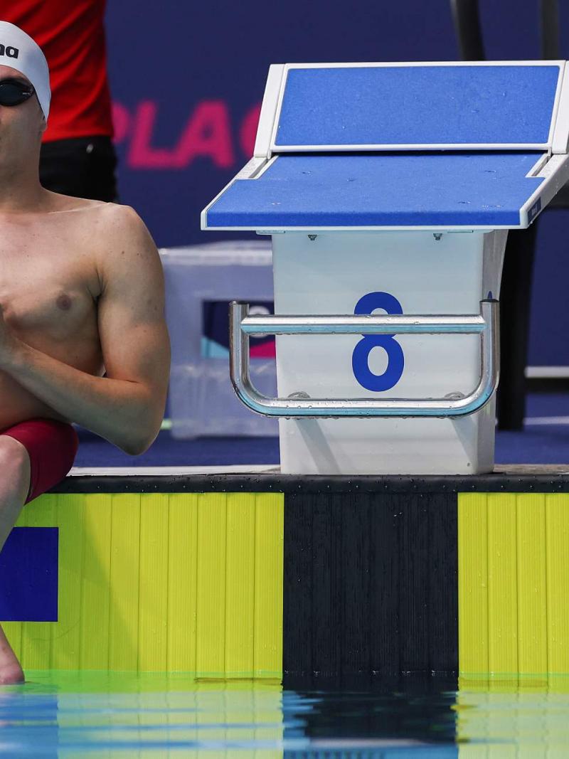 A male Para swimmer seated next to a starting block by a swimming pool