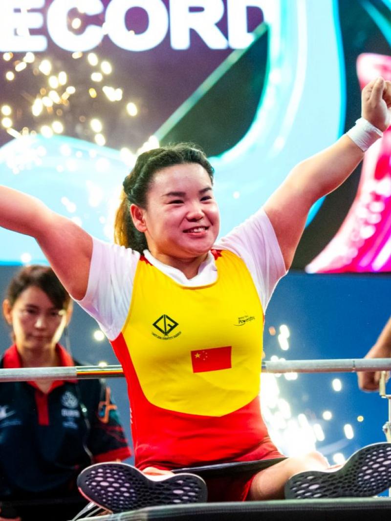 A female athlete on a bench press celebrating with two people in the background