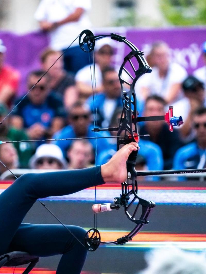 A female athlete without arms aims her shot by holding the bow with her right leg.